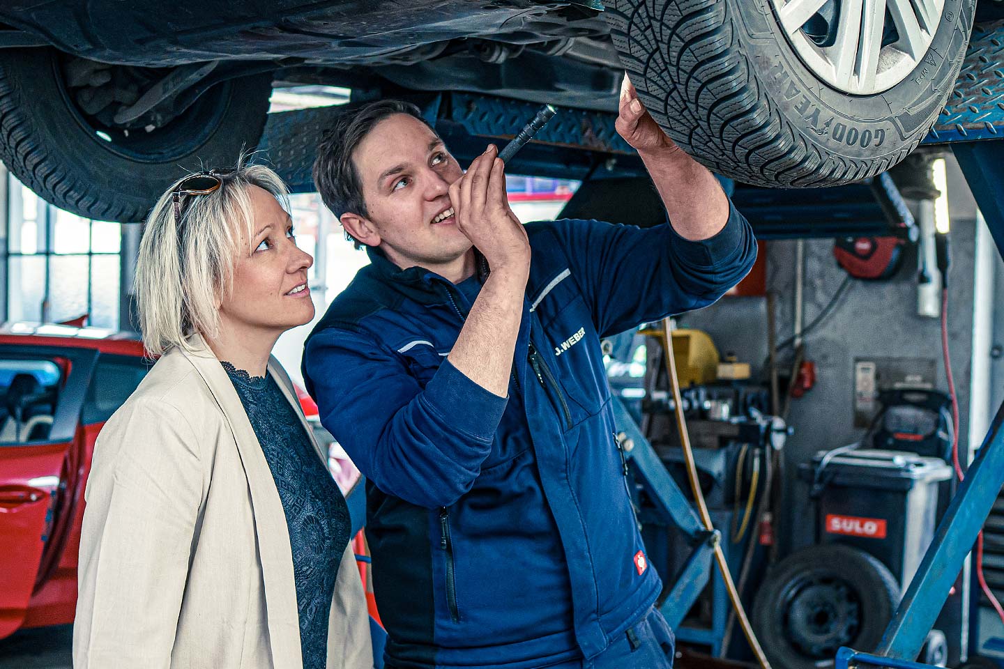 Mechaniker zeigt Kundin den Zustand des Fahrzeugs unter der Hebebühne