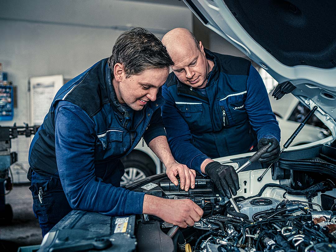 Zwei Kfz-Mechaniker arbeiten gemeinsam am Motor eines Kundenfahrzeugs
