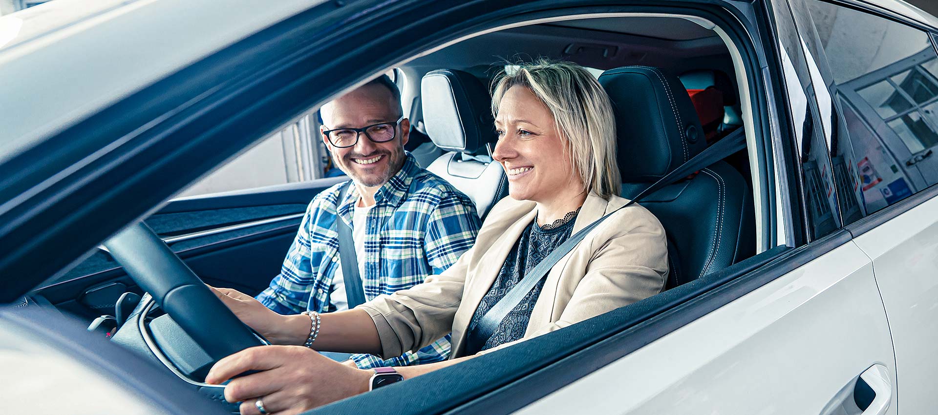 Kunde und Kundin sitzen lächend im Fahrzeug und freuen sich über das reparierte Auto